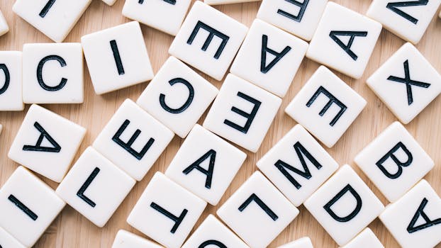 A close-up of scattered letter tiles on a wooden surface, captured from above.