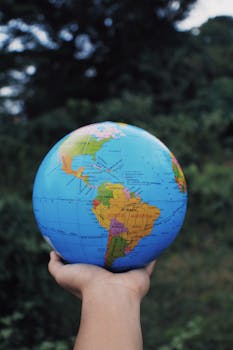 pexels photo 7425352 7425352 Crop anonymous person reaching out hand and showing Earth globe against green plants in daytime